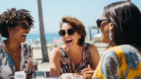 Three happy women laughing together at a cafe by a beach
