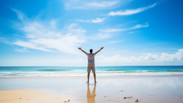Man in a great mood standing on a beach with outstretched arms.